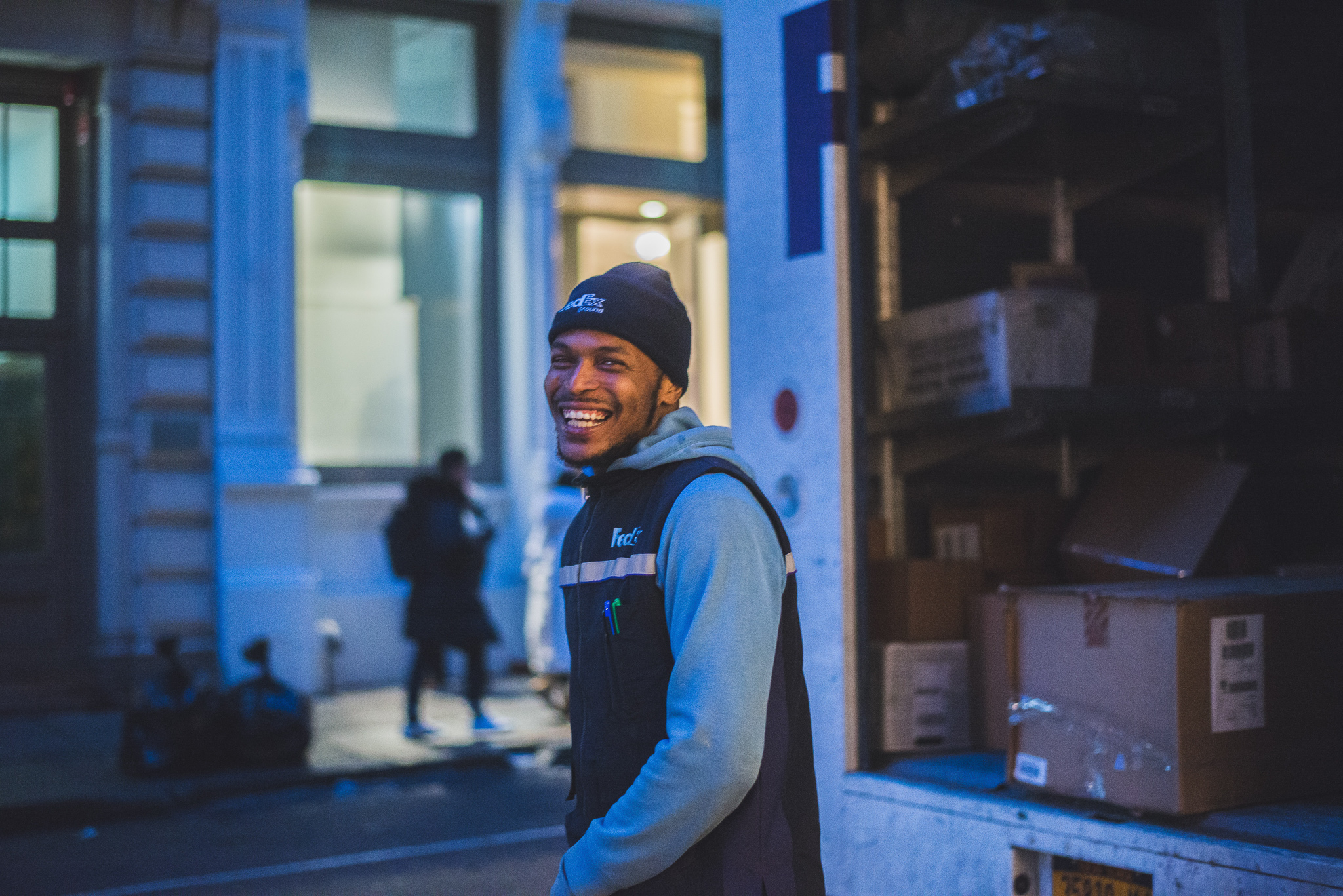 Man in a bennie standing outside of a truck with boxes inside.